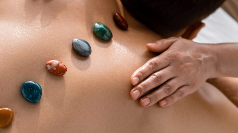 panoramic shot of masseur and shirtless man with stones on back