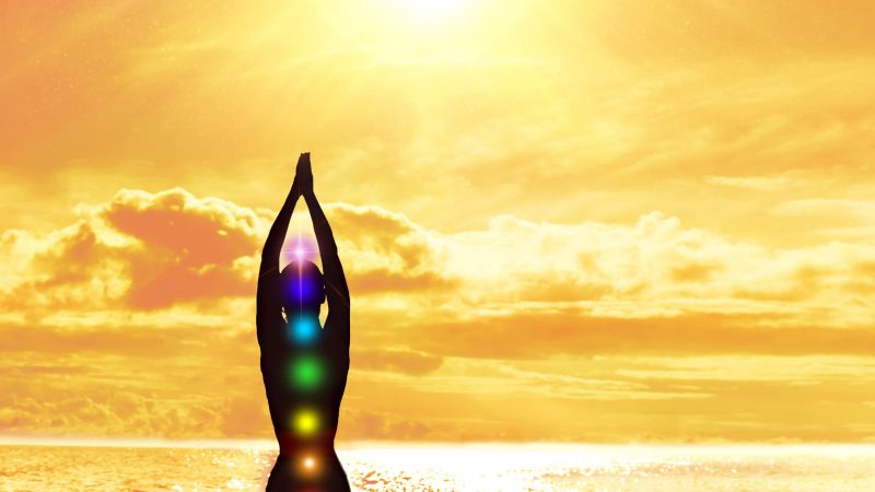 Chakras. Silhouette of a woman with hands up on the background of the sea and the sun. Harmony concept