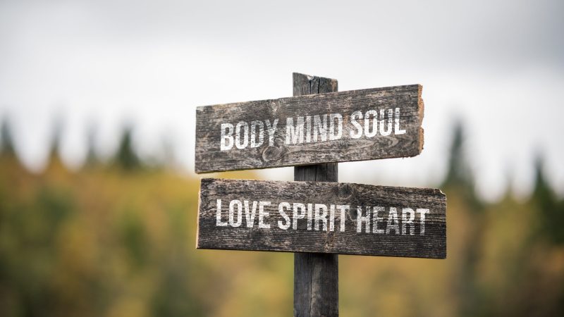 vintage and rustic wooden signpost with the weathered text quote body mind soul love spirit heart, outdoors in nature.