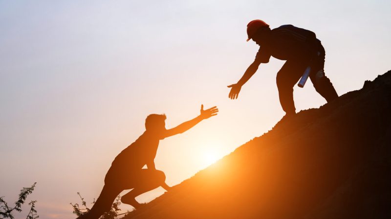 Tourists go up the hill in the sunrise to shake hands The male traveler shakes the hand of the male traveler who is climbing to the top of the hill