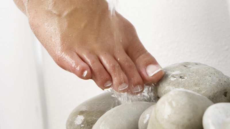 Water pouring down on woman's foot and stones